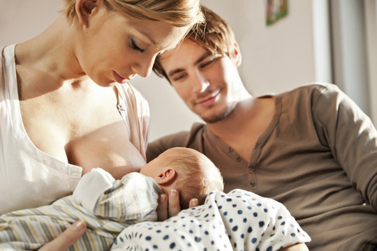 Mother breastfeeding her newborn baby with father watching