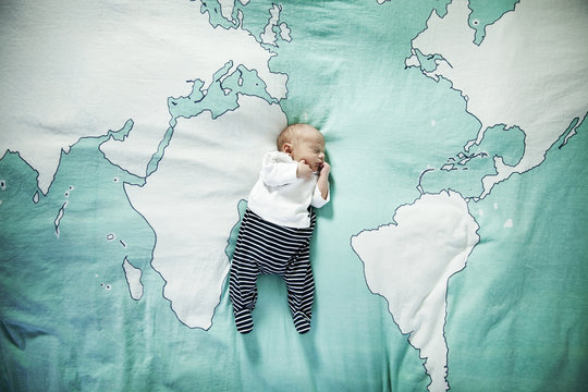 Newborn baby sleeping on blanket with world map