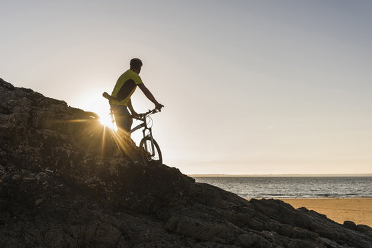 France, Crozon peninsula, mountain biker looking at sunset