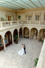 Obraz premium Wedding couple indoors is hugging each other. Beautiful model girl in white dress. Man in suit. Beauty bride with groom. Female and male portrait. Woman with lace veil. Cute lady and handsome guy