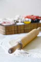Dough and rolling pin on the white table with blurred ingredients