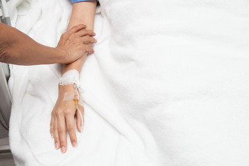 Friendly female hands holding patient hand lying in bed for enco
