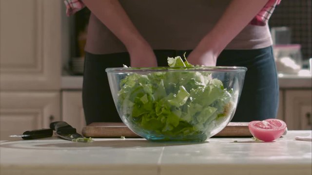 Woman puts sliced lettuce into the salad-bowl