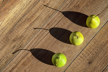 Three juicy green pear with water drops cast a long shadows on wood background 