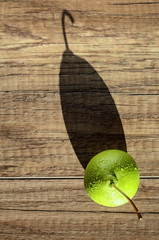 Swadow from pear. Alone juicy green pear with water drops cast a long shadow on wood background 