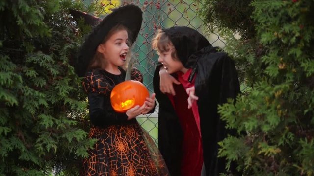 Children wearing witch costumes with hats playing with pumpkin with a burning candle in autumn Park on Halloween. boy and girl scare each other. Kids trick or treat.