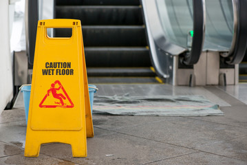 A wet floor sign and bucket at a spill in front of an escalator.