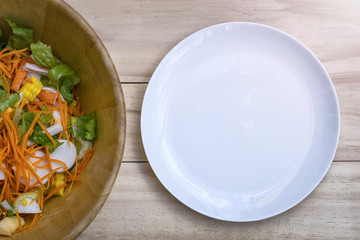 Fresh salad, fruits and greens with empty dish on wooden background top view with space for text. Healthy food.