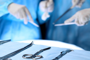 Surgical tools lying on the table while group of surgeons at background operating patient. Steel medical instruments ready to be used.