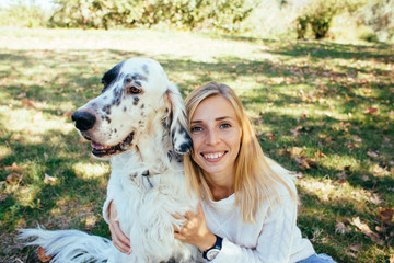 happy young woman in a white sweater and blue jeans hugging a big white dog in the park