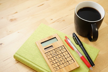 Cup of coffee with notebook and pens on wooden desk
