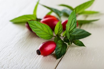 Several red hips with green herbs on white wooden board