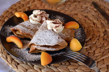 Homemade pancakes with jam, apricots, whipped cream and icing sugar.
