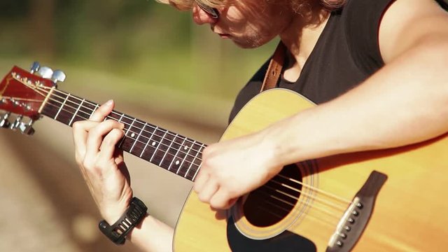 Close-up portrait of a young guitarist performing outside on acoustic guitar