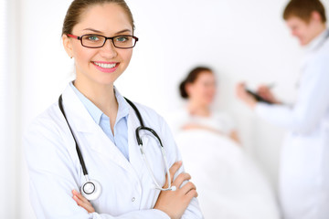 Fototapeta premium Cheerful smiling female doctor on the background with physician and his patient in the bed. High level and quality of medical service concept.