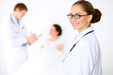 Fototapeta premium Cheerful smiling female doctor on the background with physician and his patient in the bed. High level and quality of medical service concept.