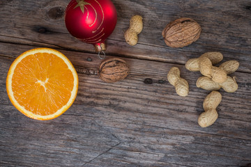 Fototapeta na wymiar Weihnachtshintergrund: Orange, Nüsse und Christbaumkugel auf Holzuntergrund