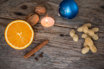 Weihnachtshintergrund: Orange, Zimt, Nelken, Nüsse, Christbaumkugel und Teelicht auf Holzuntergrund