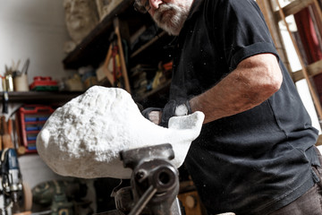 Senior sculptor working on his marble sculpture in his workshop with hammer and chisel.