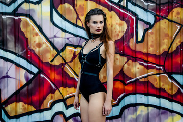 Attractive young girl with long hair wearing body posing on a background of wall with graffiti