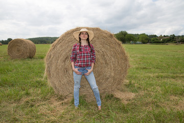 Naklejka na ściany i meble Full length portrait of beautiful countrywoman standing next to hay stack