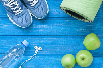 Flat lay sport shoes, bottle of water, mat and earphones on blue