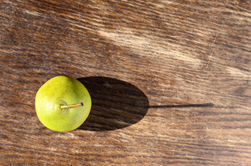 Swadow from pear. Alone juicy green pear with water drops cast a long shadow on wood background 