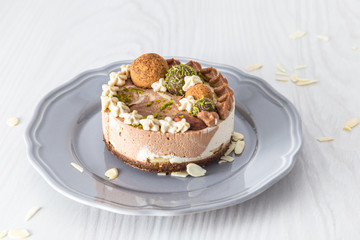 Raw vegan cake with lime, banana and chocolate, decorated with lime zest and chocolate balls on a grey plate on a light background 