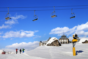 Chair-lift in blue sky and three skiers on ski slope at sun nice