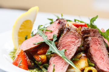 Roast beef with arugula, vegetables and lemon sliced, lies on th