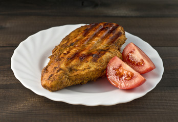 grilled chicken breast with tomatoes served on white plate on wooden table
