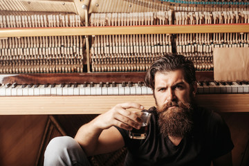 bearded man with glass near wood piano