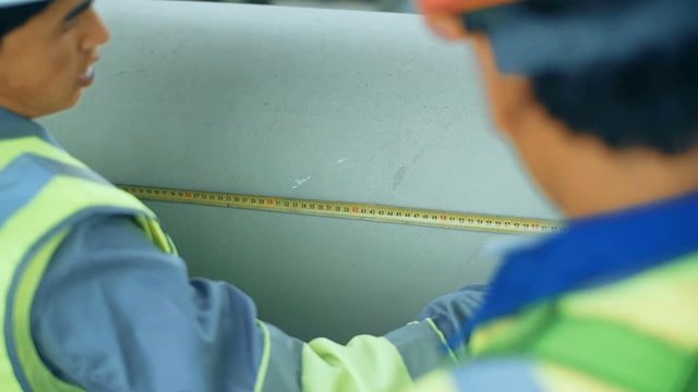 Workers measuring a tube with a tape measure. Industrial back ground with gas pipiline