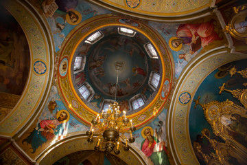 Fototapeta na wymiar Dome of the church painted frescoes depicting holy martyrs. a large chandelier hanging in the center.