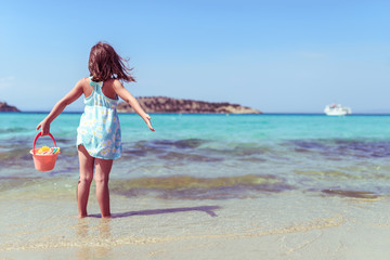 Little Girl Standing on the Beach With Sand Toys Looking at Sea