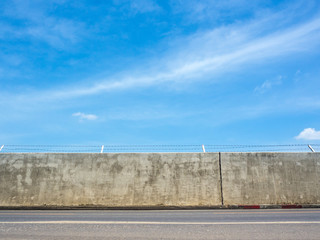 Fototapeta na wymiar Concrete wall street with barbed wire fence under a blue sky and