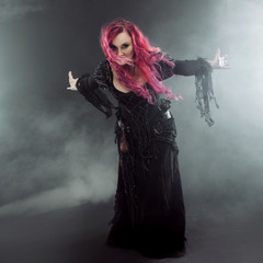 Fototapeta premium Halloween Witch creates magic. Attractive woman with red hair in witches costume standing outstretched arms, strong wind