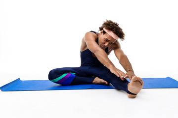 Sportive african man stretching, sitting on karemat over white background.