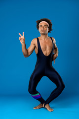 Sportive african man training, fooling, showing peace over blue background.