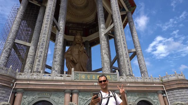 Young caucasian man taking selfie with Guan Yin statue