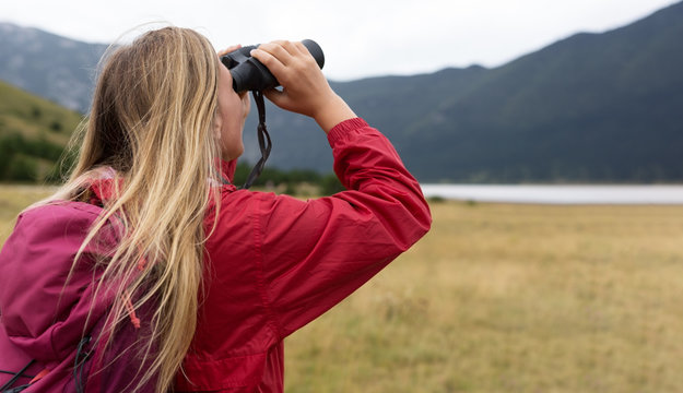 young blonde woman hiking and watching through binoculars.