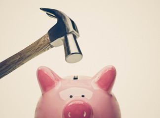 A sad pink piggy bank is about to be hit by a hammer in old vintage tone / Financial problem