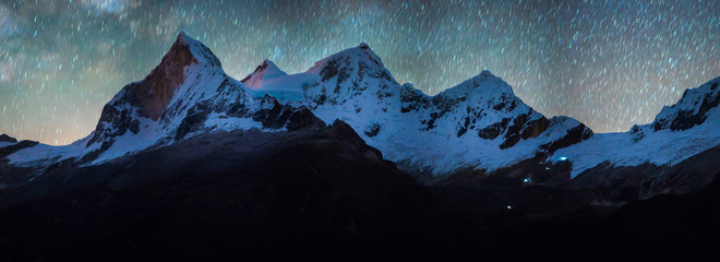 The  startrail over tha Huandoy mountain and a group of climbers starting their journey at dawn.