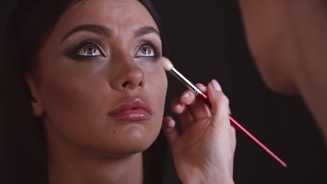 Closeup of face of young attractive woman looking up while professional doing make up for her