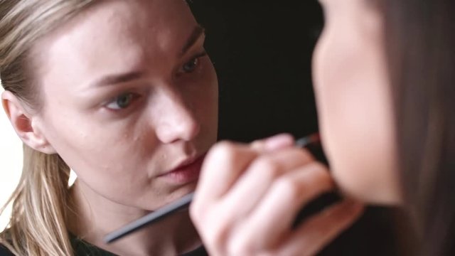 Woman makeup artist applying lipstick to lips of model in studio