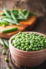 Green peas in wooden bowl on  rural background