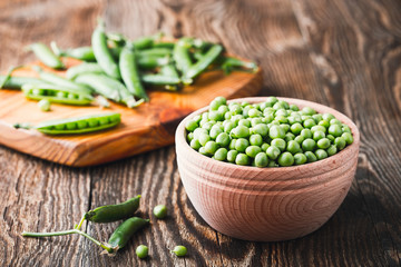 Green peas in wooden bowl on  rural background