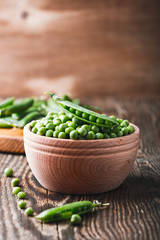 Green peas in wooden bowl on  rural background