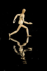Holzfigur rennt durch Wasser, Spiegelung in der Pfütze