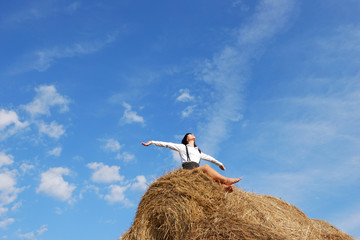 Woman on hay bale in summer field enjoying a warm windy day